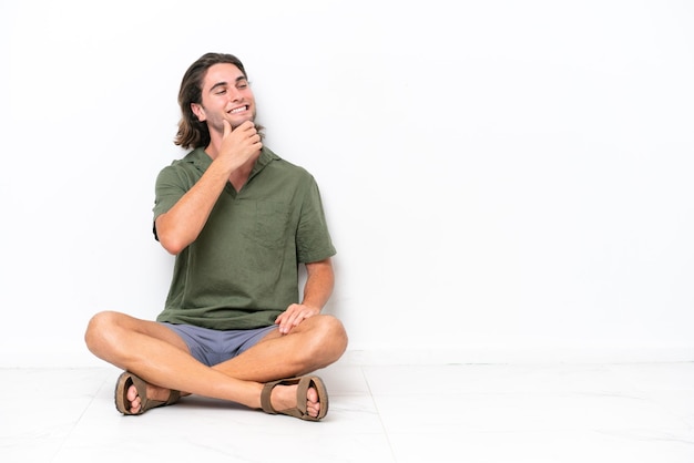 Young handsome man sitting on the floor isolated on white background looking to the side