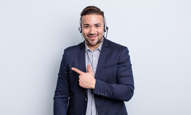 young handsome man smiling cheerfully, feeling happy and pointing to the side. telearketer concept