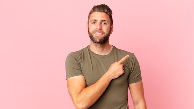 Young handsome man smiling cheerfully, feeling happy and pointing to the side