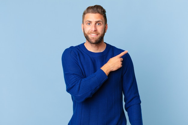 Young handsome man smiling cheerfully, feeling happy and pointing to the side