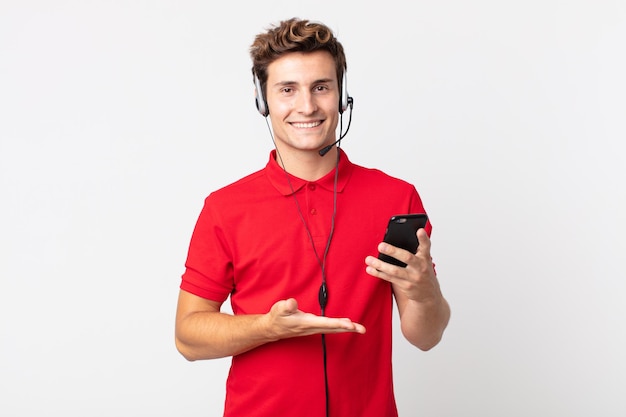 Young handsome man smiling cheerfully, feeling happy and showing a concept with a smartphone and headset