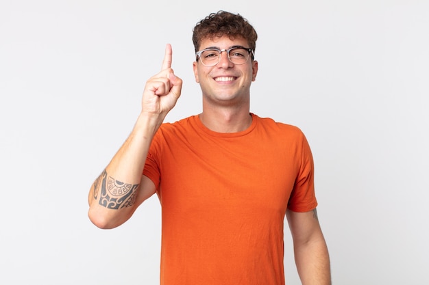 Young handsome man smiling cheerfully and happily, pointing upwards with one hand to copy space