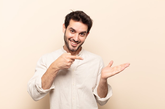 Young handsome man smiling cheerfully and pointing to copy space on palm on the side, showing or advertising an object