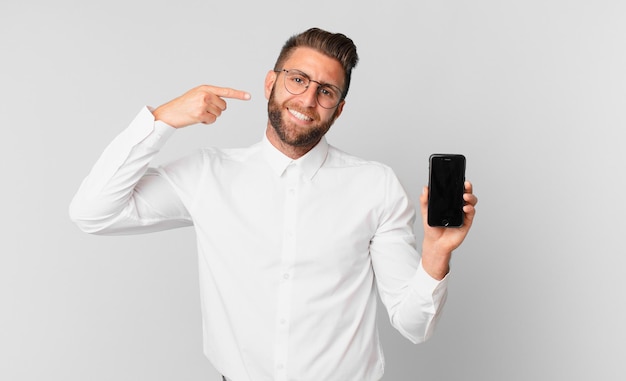 young handsome man smiling confidently pointing to own broad smile and holding a cell