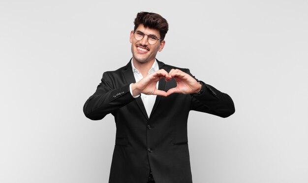 Young handsome man smiling and feeling happy, making heart shape with both hands