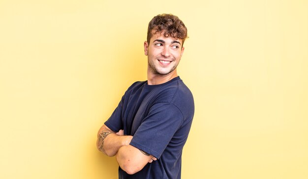 Young handsome man smiling gleefully, feeling happy, satisfied and relaxed, with crossed arms and looking to the side