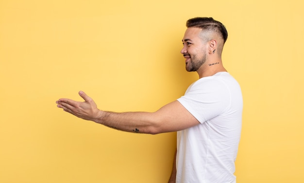 Photo young handsome man smiling, greeting you and offering a hand shake to close a successful deal, cooperation concept