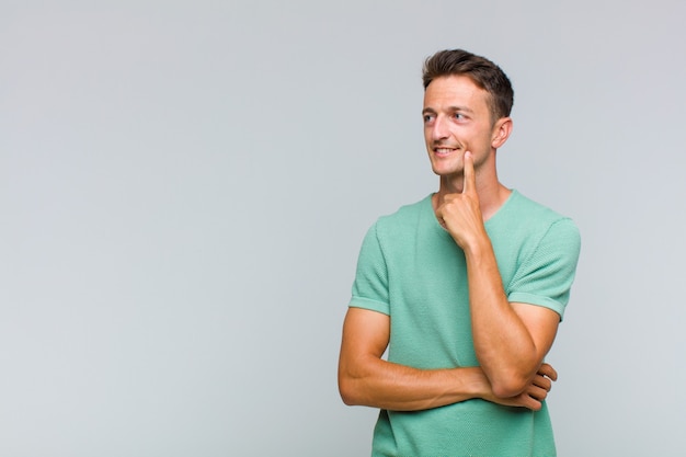 Young handsome man smiling happily and daydreaming or doubting, looking to the side