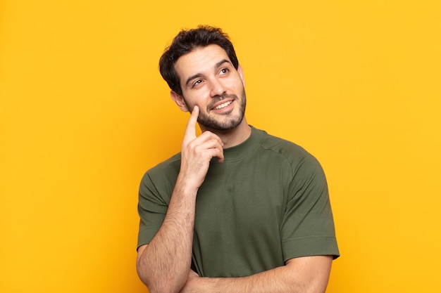 Young handsome man smiling happily and daydreaming or doubting