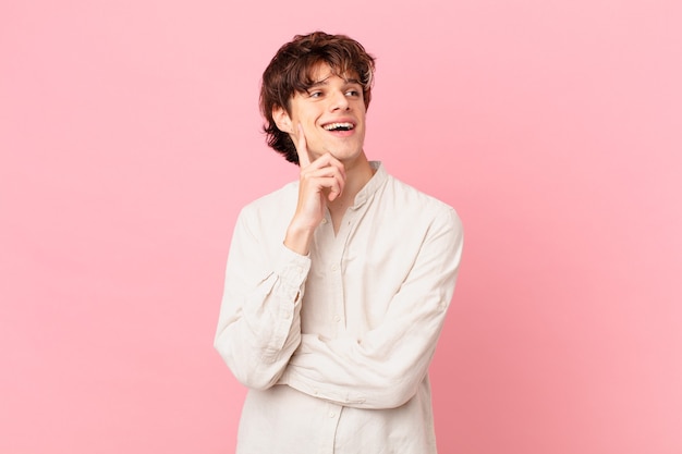 Young handsome man smiling happily and daydreaming or doubting