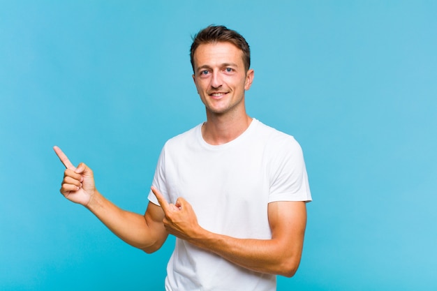 Young handsome man smiling happily and pointing to side and upwards with both hands showing object in copy space