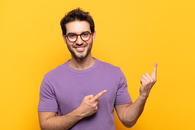 Young handsome man smiling happily and pointing to side and upwards with both hands showing object in copy space