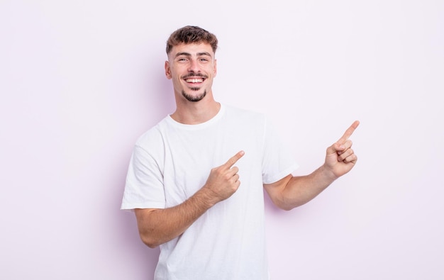 young handsome man smiling happily and pointing to side and upwards with both hands showing object in copy space