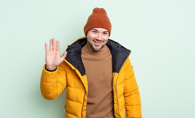 Photo young handsome man smiling happily waving hand welcoming and greeting you cold weather concept