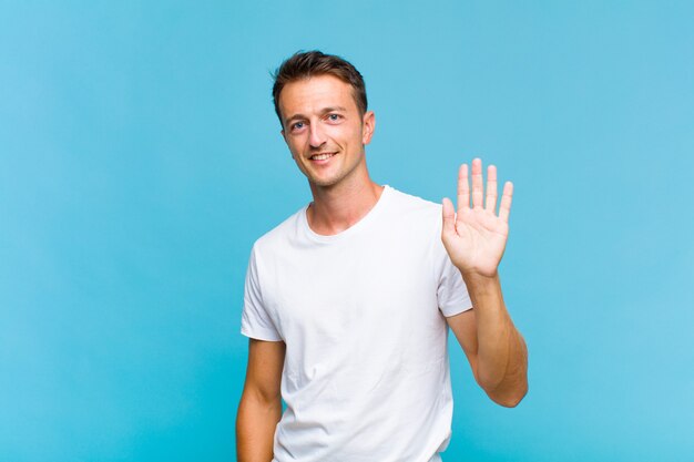 Young handsome man smiling happily and waving