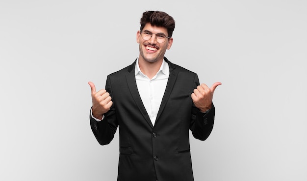 Young handsome man smiling joyfully and looking happy, feeling carefree and positive with both thumbs up