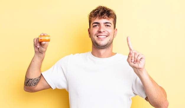 Young handsome man smiling and looking friendly, showing number one with a battery