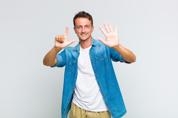 Young handsome man smiling and looking friendly, showing number seven or seventh with hand forward, counting down