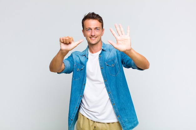 Young handsome man smiling and looking friendly, showing number six or sixth with hand forward, counting down