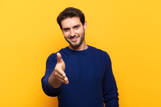 Young handsome man smiling, looking happy, confident and friendly, offering a handshake to close a deal, cooperating