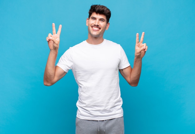 Young handsome man smiling and looking happy, friendly and satisfied, gesturing victory or peace with both hands