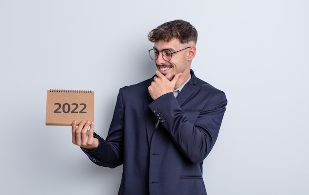 young handsome man smiling with a happy, confident expression with hand on chin. calendar concept