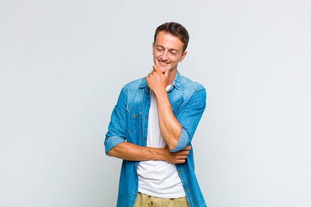 Young handsome man smiling with a happy, confident expression with hand on chin, wondering and looking to the side