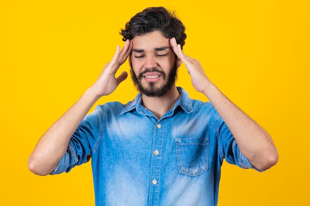 Young handsome man standing over isolated yellow background suffering from headache desperate and stressed because pain and migraine Hands on your head