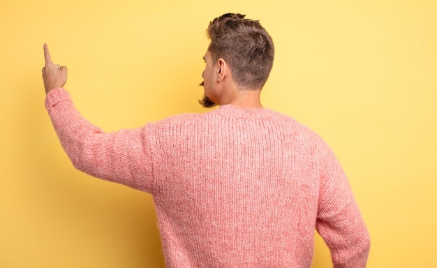 Photo young handsome man standing and pointing to object on copy space rear view strange moustache concept