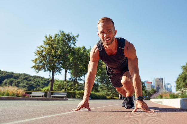 Young handsome man in a starting position for running on a sports track