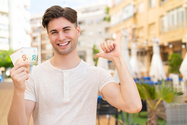 Young handsome man taking a lot of money at outdoors proud and selfsatisfied