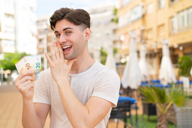 Young handsome man taking a lot of money at outdoors whispering something