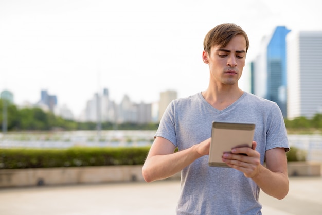 Young handsome man using digital tablet while relaxing at the pa