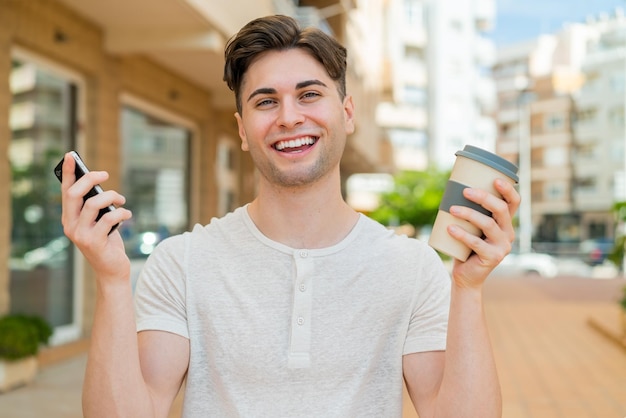 Young handsome man using mobile phone and holding a coffee with happy expression