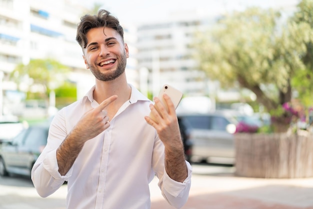 Young handsome man using mobile phone at outdoors and pointing it