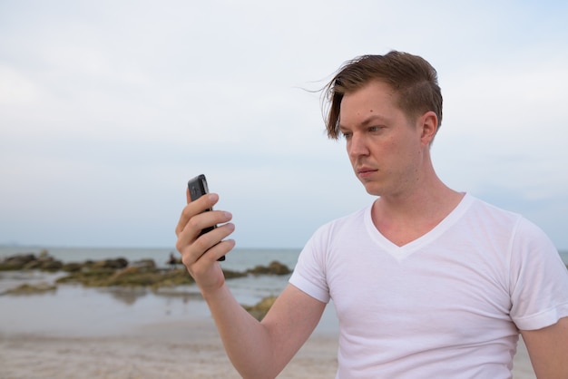 Young handsome man using mobile phone at the public beach