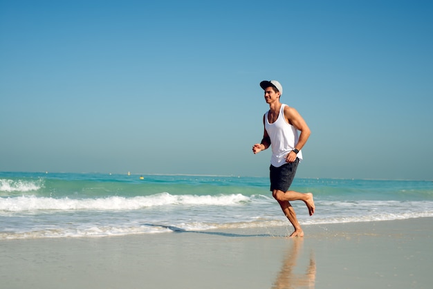 Young handsome man wearing a cap while running on the beach.