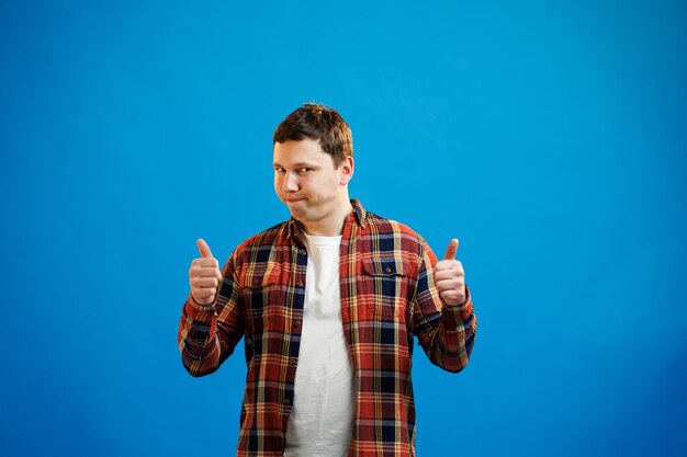 Young handsome man wearing casual shirt over blue background approving doing positive gesture with hand thumbs up smiling and happy for success Winner gesture