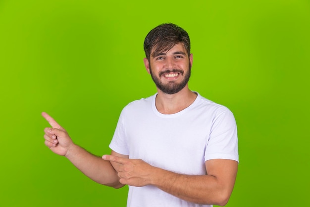 Young handsome man wearing casual white tshirt smiling and looking at the camera pointing with copy space