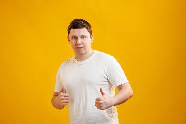 Young handsome man wearing white tshirt over yellow background approving doing positive gesture with hand thumbs up smiling and happy for success Winner gesture