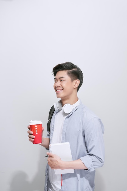 Young handsome man with backpack holding smart phone and coffee isolated on white background. Smiling student or businessman studio portrait