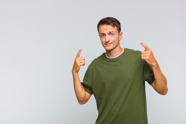 Young handsome man with a bad attitude looking proud and aggressive, pointing upwards or making fun sign with hands