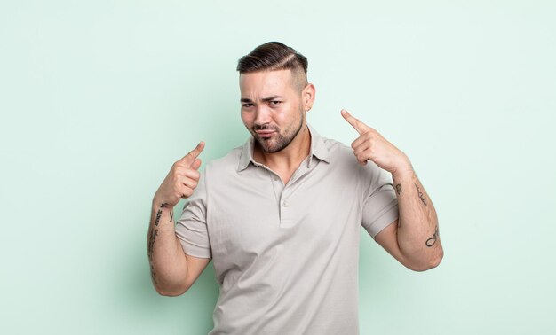 Young handsome man with a bad attitude looking proud and aggressive, pointing upwards or making fun sign with hands