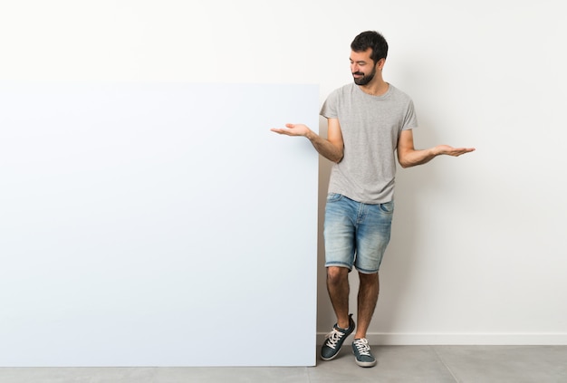 Photo young handsome man with beard holding a big blue empty placard holding copyspace with two hands