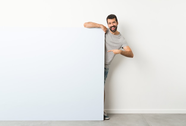 Young handsome man with beard holding a big blue empty placard and pointing it