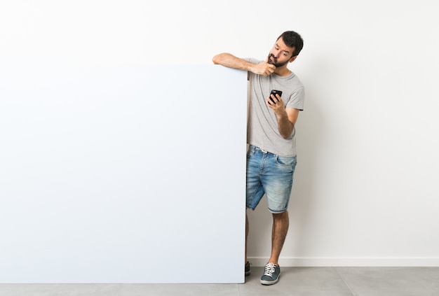 Young handsome man with beard holding a big blue empty placard thinking and sending a message