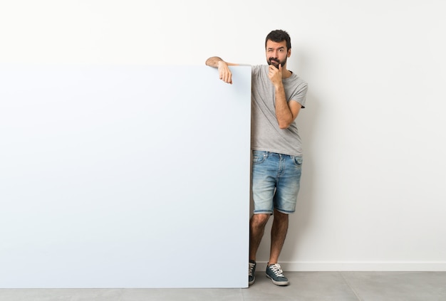 Young handsome man with beard holding a big blue empty placard thinking