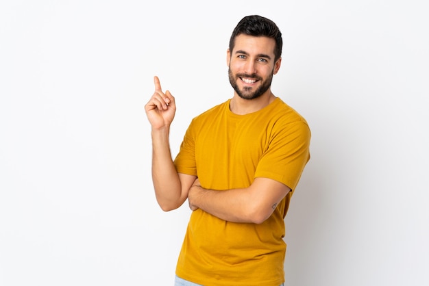 Young handsome man with beard isolated on white wall happy and pointing up