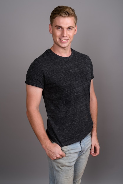 Young handsome man with blond hair wearing gray shirt on grey wall