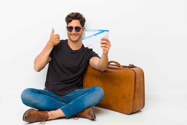 Young handsome man with a boarding pass tickets sitting on the floor in a white room